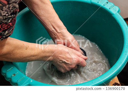 Grandma washes clothes in a poor neighborhood.Hand washing of household clothes 136900170