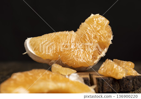 half of an orange citrus on a wooden board, ripe sweet and juicy citrus on a table made of pine wood, close up 136900220