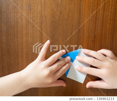 Child's hands folding blue origami paper on a wooden table 136901213