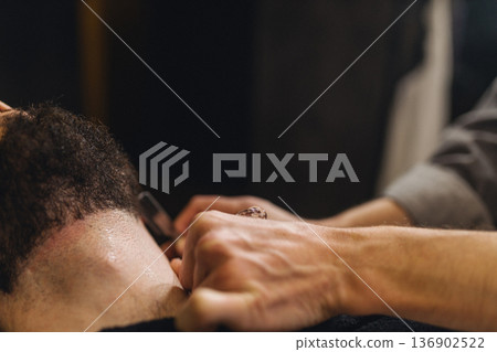 Close up of professional barber shaving male neck with straight razor in barbershop. Beard contouring, classic wet shave, men grooming service and barber work process concept. Close up of professional barber shaving male neck with straight razor in barbershop. Beard contouring, classic wet shave, men grooming service and barber work process concept. 136902522