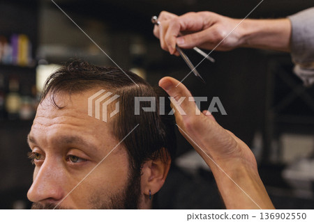 Barber cutting male client hair with scissors and comb. Close up of professional haircut process, precision technique, men grooming service in modern barbershop. 136902550