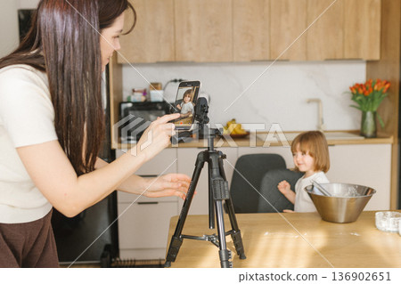 Mother recording daughter cooking on smartphone in kitchen, family creating home video content and baking together Mother recording daughter cooking on smartphone in kitchen, family creating home video content and baking together 136902651