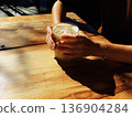 Photo of a person holding an iced latte in a cafe with sunlight filtering through the trees 136904284