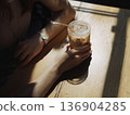 Photo of a person holding an iced latte in a cafe with sunlight filtering through the trees 136904285