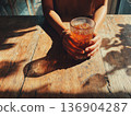 Photo of a person holding an iced latte in a cafe with sunlight filtering through the trees 136904287