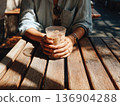 Photo of a person holding an iced latte in a cafe with sunlight filtering through the trees 136904288