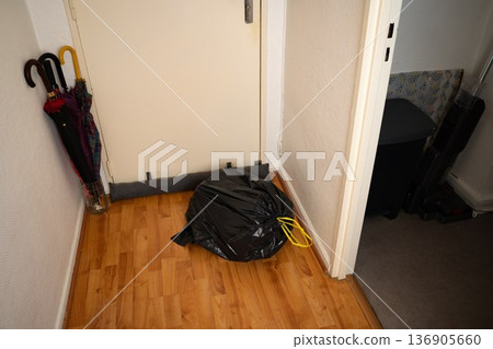 Full black trash bag on the corridor floor next to an interior door in a casual home setting. Domestic scene waste management and household routine. Concept of cleaning, domestic, organization. 136905660