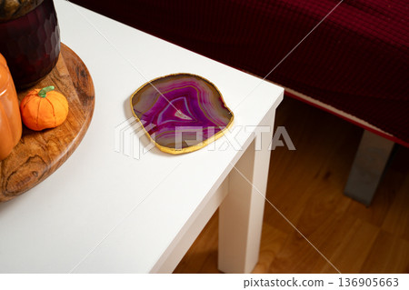 Pink agate coaster placed on the side of a white coffee table in a simple, everyday home interior, combining natural stone and clean modern decor. Energy, grounding, spirituality, minimalism 136905663