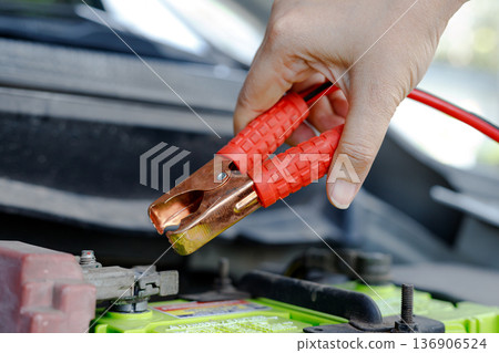 Hand holding jumper cable clamp near car battery Hand holding jumper cable clamp near car battery 136906524