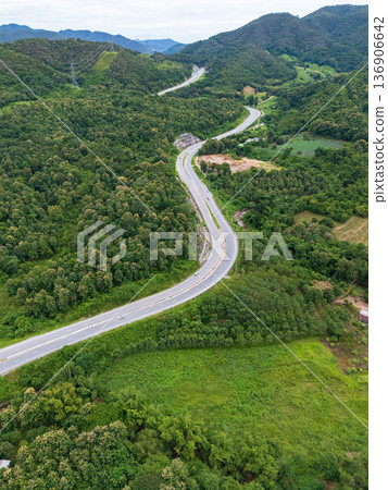 Aerial drone view of Highway 101 winding through lush green mountains between Phrae and Nan, Thailand. A scenic landscape of the road surrounded by tropical forest and a peaceful countryside Aerial drone view of Highway 101 winding through lush green mountains between Phrae and Nan, Thailand. A scenic landscape of the road surrounded by tropical forest and a peaceful countryside 136906642