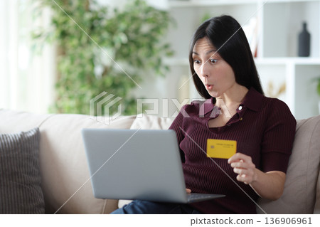 Surprised asian woman paying online with card and computer Surprised asian woman paying online with card and computer 136906961