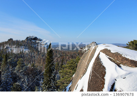 Snow capped mountains and evergreen forest under clear blue sky in Krasnoyarsk Pillars national park landscape. Siberian wilderness view. 136907678