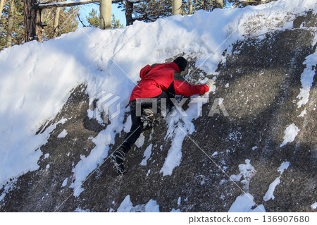 Man scaling a snow-covered rock in Krasnoyarsk Pillars national park. Winter climbing and outdoor adventure in a natural landscape for extreme sport. Man scaling a snow-covered rock in Krasnoyarsk Pillars national park. Winter climbing and outdoor adventure in a natural landscape for extreme sport. 136907680