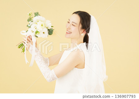 Portrait of a young bride wearing a wedding dress and holding a bouquet against a beige background 136907793