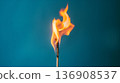 Lively flame of a single matchstick burns brightly against a cool blue background, representing ignition and energy. 136908537