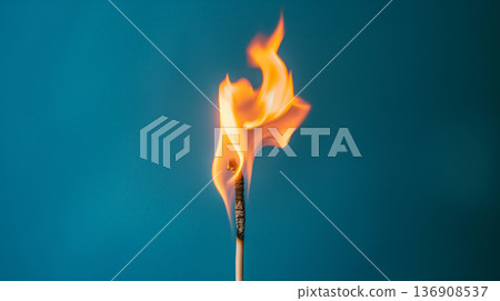 Lively flame of a single matchstick burns brightly against a cool blue background, representing ignition and energy. 136908537