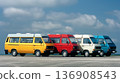 Vibrant lineup of classic yellow, red, blue, and white vans parked neatly against a clear blue sky. 136908543