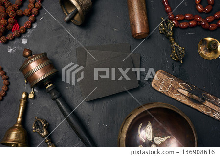 Blank black business cards in the center surrounded by a Tibetan singing bowl, prayer drum, bells, rosary beads and ritual objects 136908616