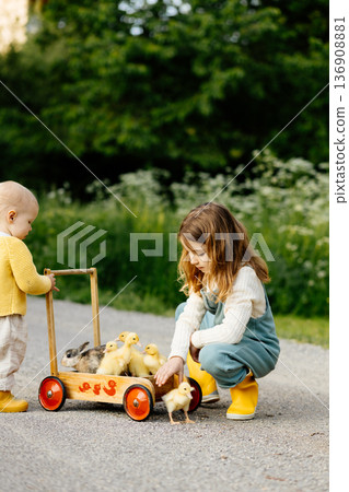 Sisters carrying ducklings and baby bunnies on wooden toy cart. 136908881