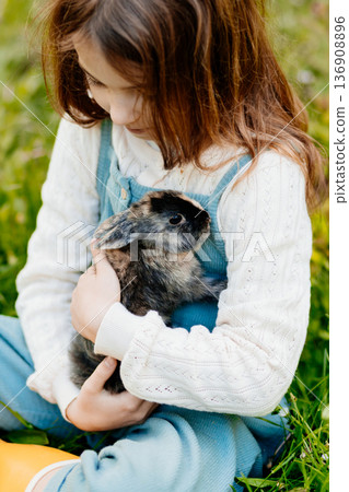 Young girl gently cuddles a fluffy bunny in her arms. 136908896