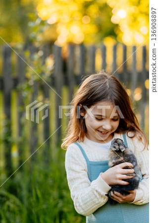Young girl gently cuddles a fluffy bunny in her arms. 136908897