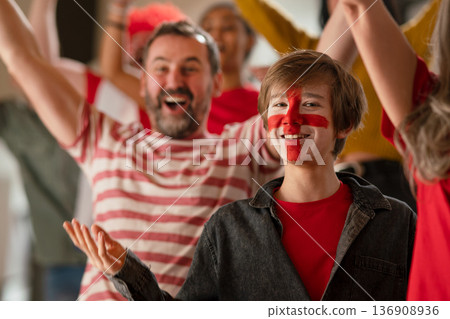 Excited football fans supproting English national team in live soccer match at stadium. Excited football fans supproting English national team in live soccer match at stadium. 136908936