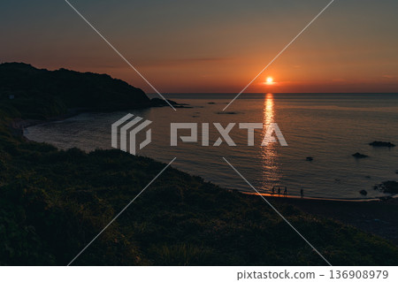 The sunset-colored beach and the silhouettes of people standing 136908979