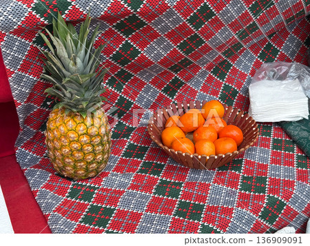 Pineapple and tangerine basket on festive textile background. Tropical refreshment, market display, vitamin nutrition, and seasonal street food concept. 136909091