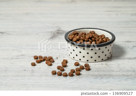 A bowl of dry dog of cat food on a gray wooden floor. 136909527