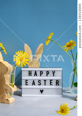 Happy Easter text on Lightbox with bunny wooden figures and fresh flowers. Easter composition content still life. Christian symbols Happy Easter text on Lightbox with bunny wooden figures and fresh flowers. Easter composition content still life. Christian symbols 136910009