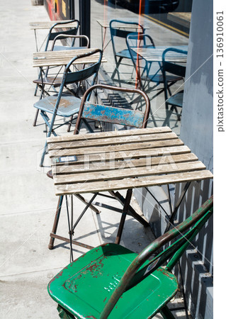 Small wooden tables and folding chairs lined up on the cobblestone sidewalk of a cafe in Shoreditch, East London 136910061