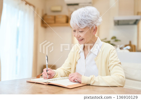 Senior Asian woman writing in a diary 136910129