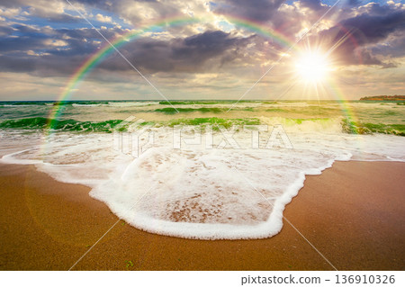 sunset over tide rolling on the sandy beach. sea waves beneath a cloudy sky. empty calm scenery in summer. loneliness concept. generic image for wallpaper or book cover use. weather with rainbow 136910326