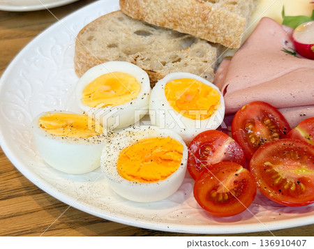 Closeup boiled eggs and tomatoes with bread on white plate. Protein nutrition, simple cooking, balanced meal, and healthy lifestyle concept. 136910407