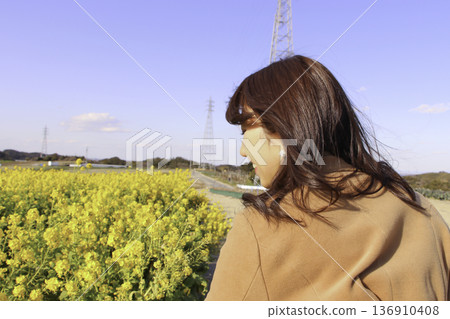 一位女子站在一片油菜花田前，背景是油菜花田。 136910408