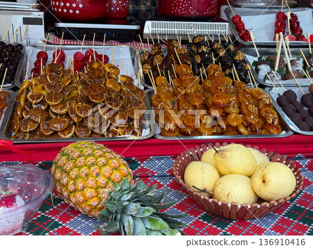 Assorted caramelized fruits and pears with pineapple on market table. Seasonal abundance, street gastronomy, harvest celebration, and traditional dessert concept. 136910416