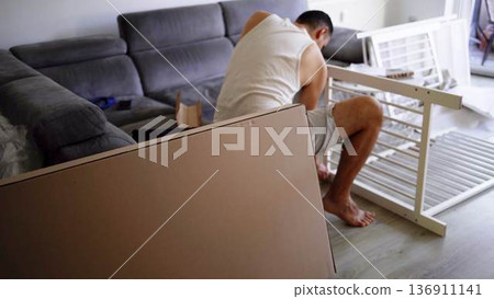 Expectant father preparing a nursery by assembling a wooden crib 136911141