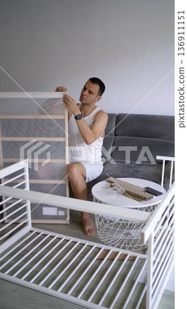 Future father assembling a white crib in a minimalist nursery ro Future father assembling a white crib in a minimalist nursery ro 136911151