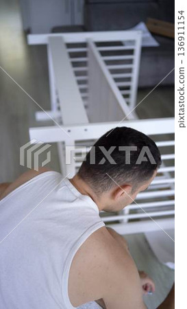 Future father assembling a white crib in a minimalist nursery ro Future father assembling a white crib in a minimalist nursery ro 136911154