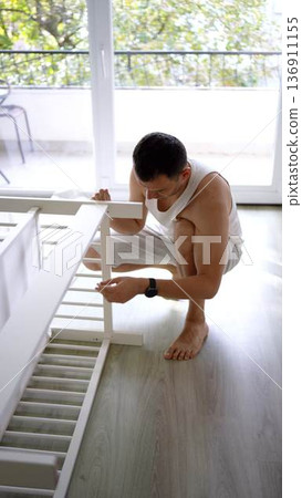 Future father assembling a white crib in a minimalist nursery ro 136911155