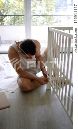 Future father assembling a white crib in a minimalist nursery ro 136911157