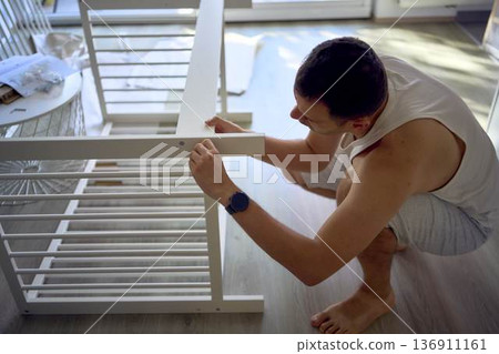 Future father assembling a white crib in a minimalist nursery room Future father assembling a white crib in a minimalist nursery room 136911161