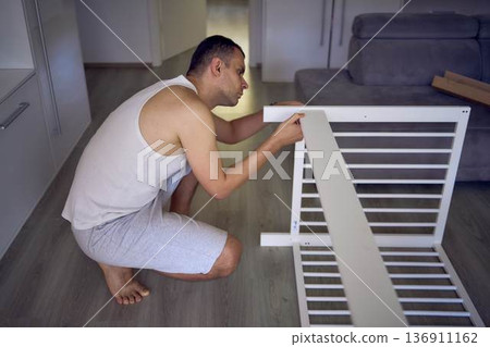 Expectant father preparing a nursery by assembling a wooden crib Expectant father preparing a nursery by assembling a wooden crib 136911162