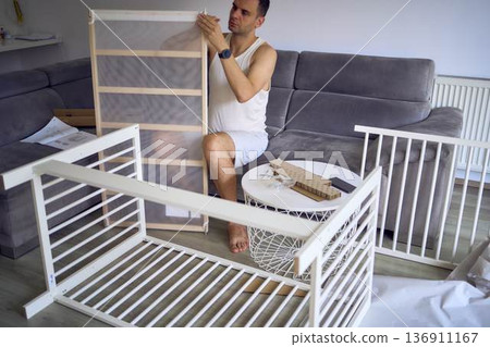 Future father assembling a white crib in a minimalist nursery room Future father assembling a white crib in a minimalist nursery room 136911167