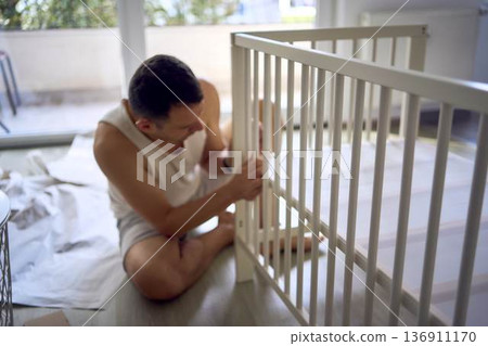 Expectant father preparing a nursery by assembling a wooden crib Expectant father preparing a nursery by assembling a wooden crib 136911170