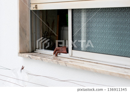 Hand reaching through a partially open window with roller shutter Hand reaching through a partially open window with roller shutter 136911345