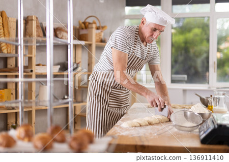 Elderly man baker cutting dough with scraper Elderly man baker cutting dough with scraper 136911410