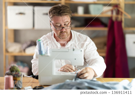 Middle-aged male dressmaker working with sewing-machine 136911411