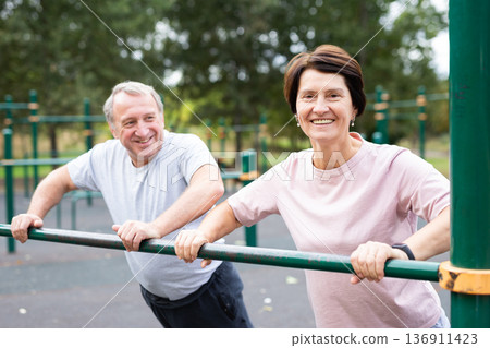 Elderly couple doing push-ups on crossbar together on sports ground of city park 136911423