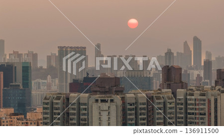 Hazy Kowloon skyline glowing under warm sunset Feb 19 2026 136911500